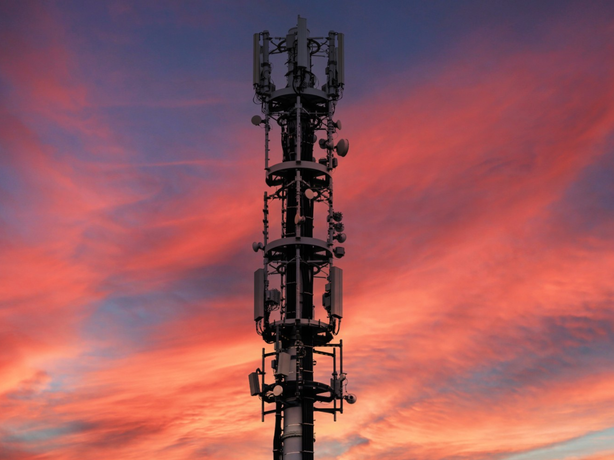 Mobile phone mast silhouetted against a pink sunset sky, illustrating the UK’s 2G network switch-off.