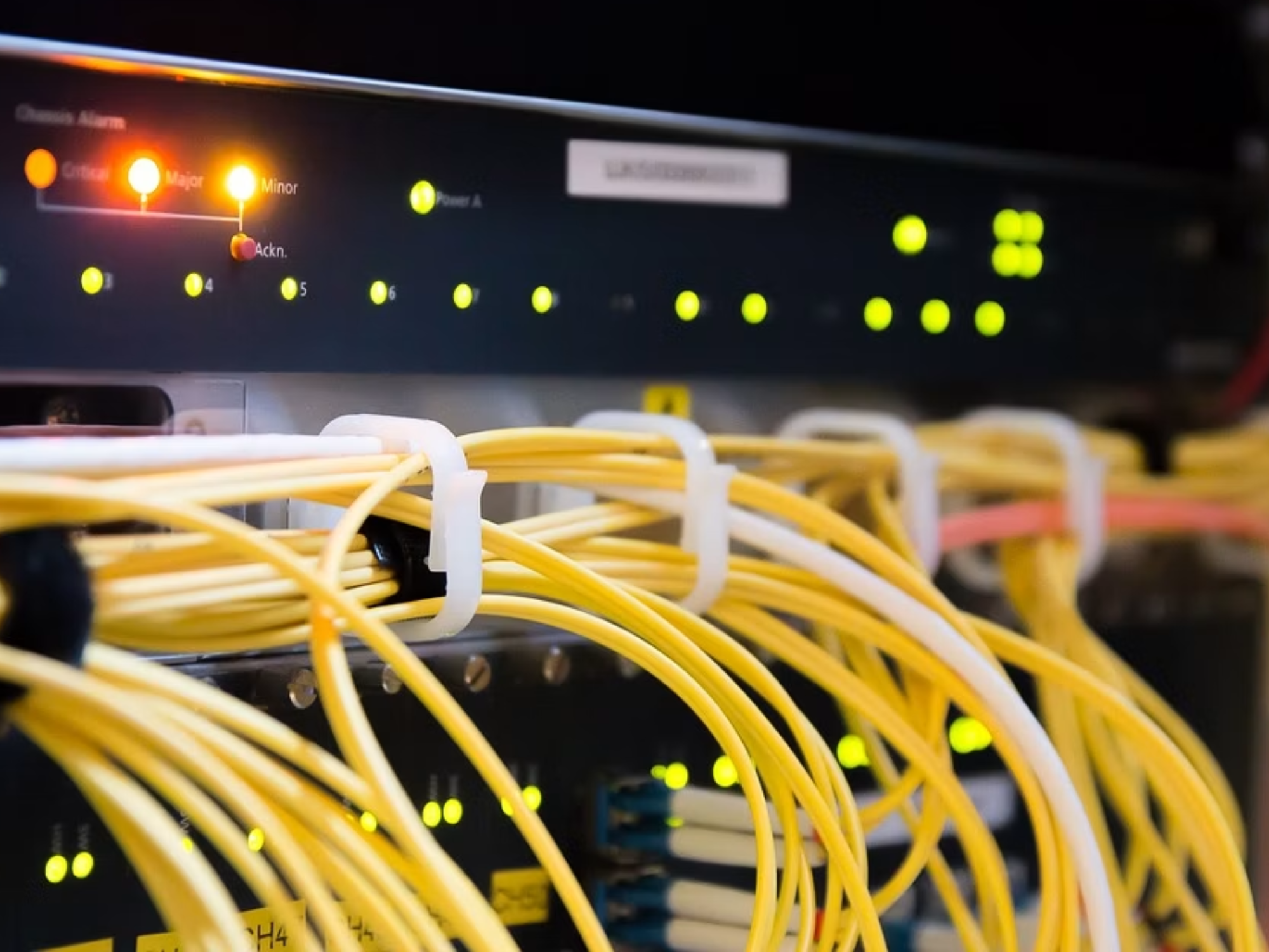 Yellow fibre optic cables connected to network equipment with illuminated status lights.