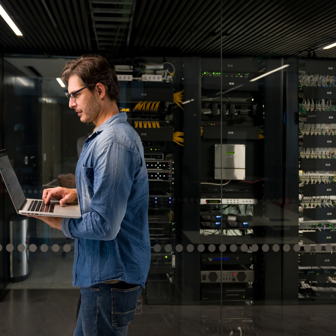 IT professional using a laptop in a server room, representing IT outages, network downtime and infrastructure troubleshooting.
