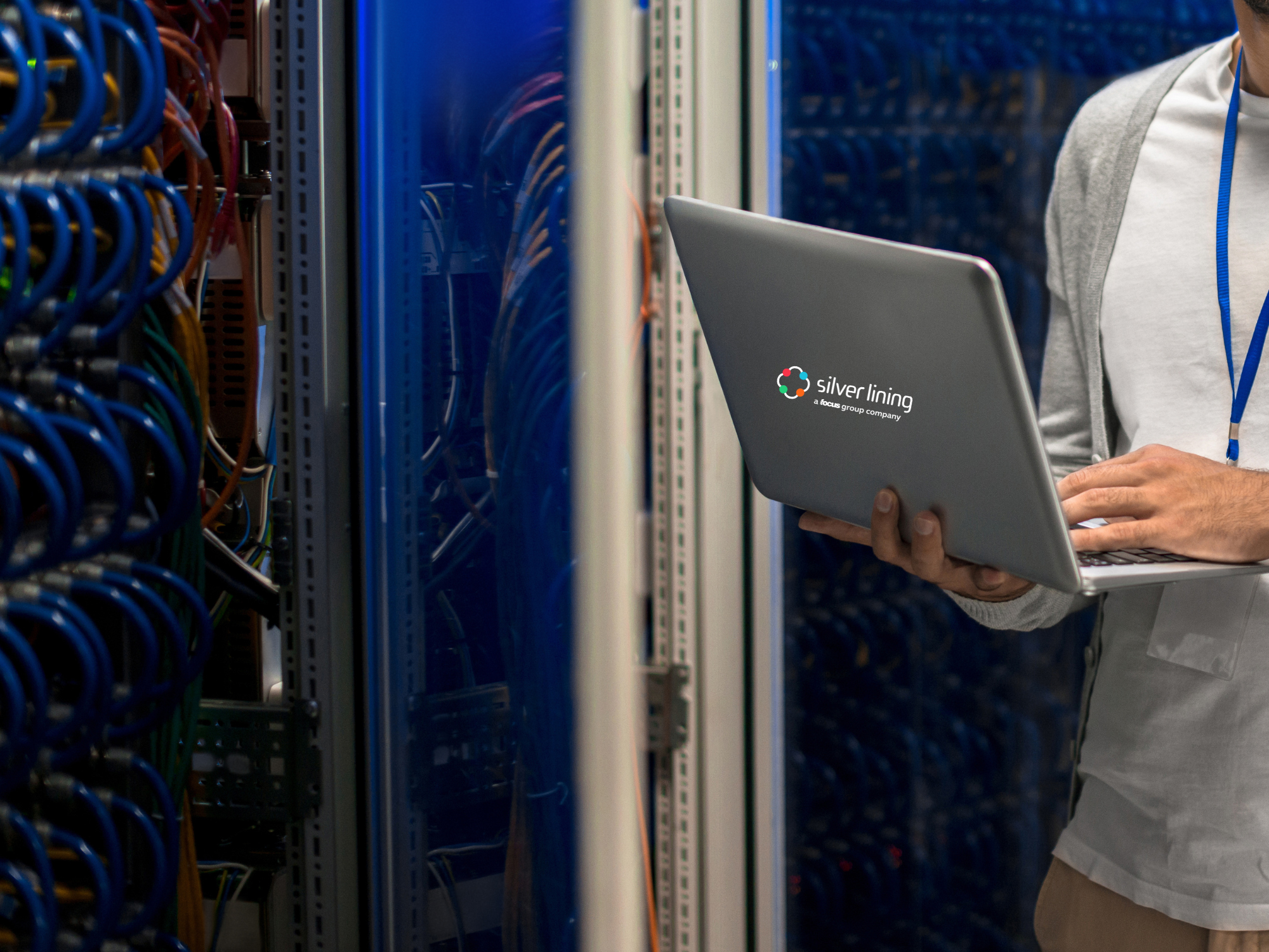 IT engineer holding a laptop with the Silver Lining logo standing in a server room beside network cabling racks.