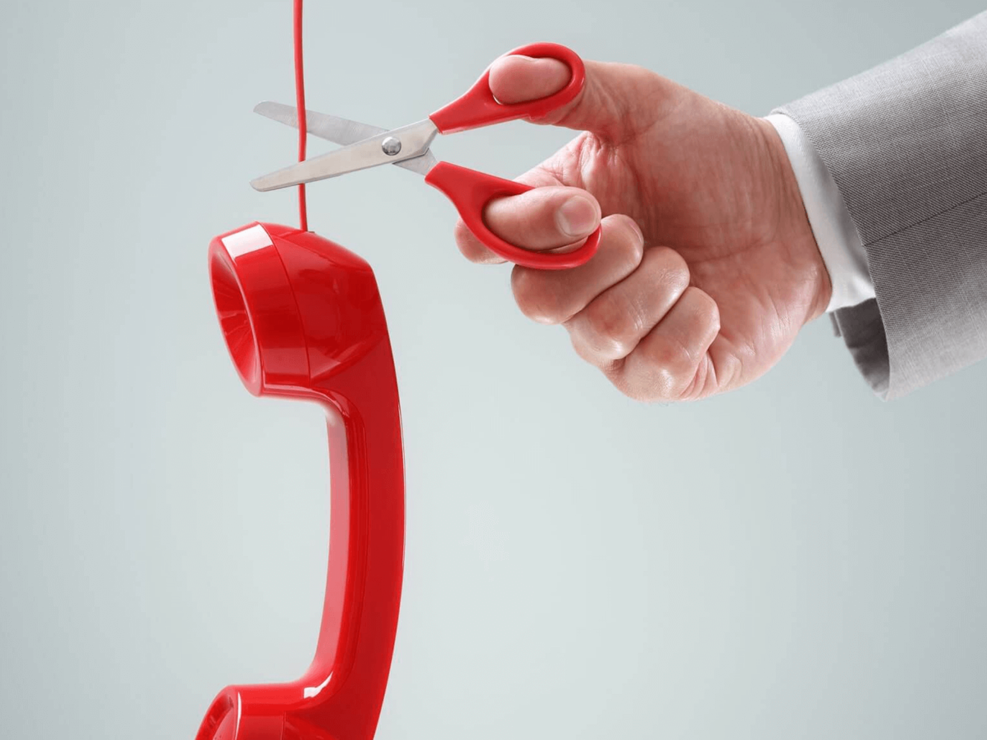 Red telephone handset cable being cut with scissors to represent the upcoming PSTN switch off and the move to modern digital phone services.