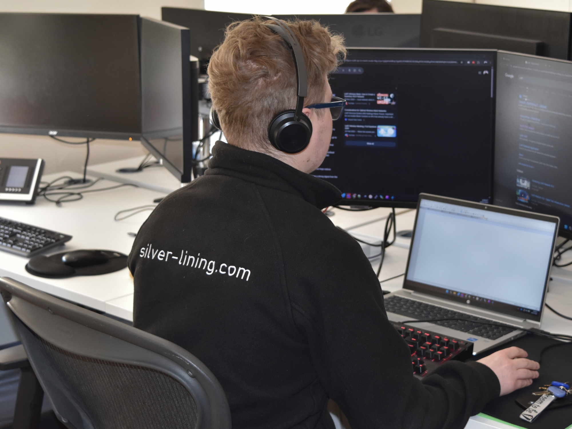 Silver Lining IT specialist wearing a wireless headset working on a laptop and multiple monitors to manage business telephony and Microsoft Teams Direct Routing.