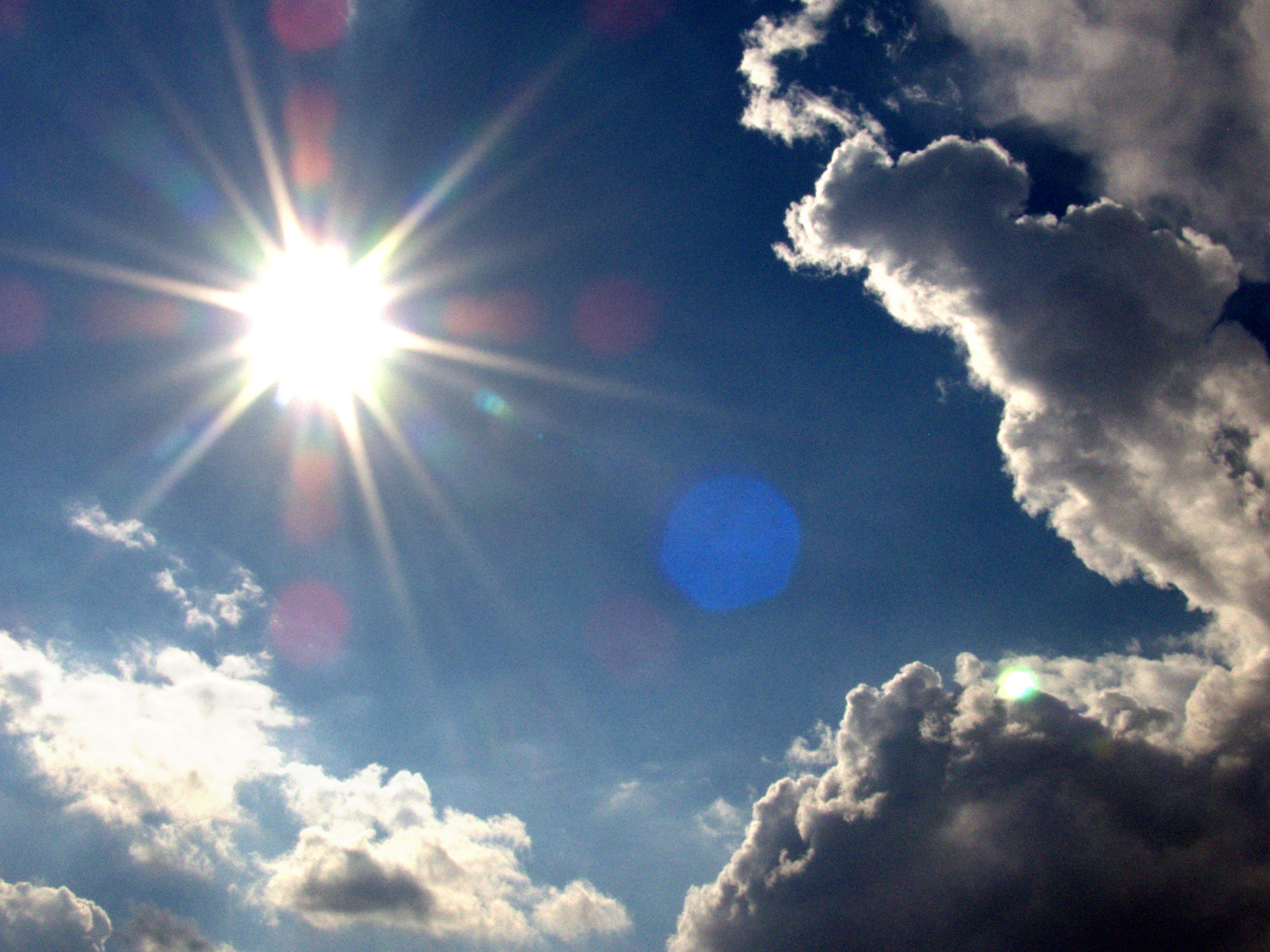 Bright sun shining through a blue sky with dark clouds, representing the impact of hot weather on IT systems.